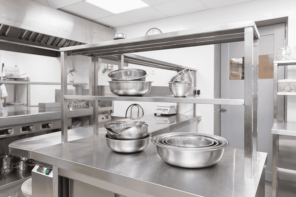 Stainless steel countertop and shelving in a commercial kitchen, featuring nested mixing bowls, precision tools, and a clean, organized layout that supports ergonomic food prep and efficient workflow