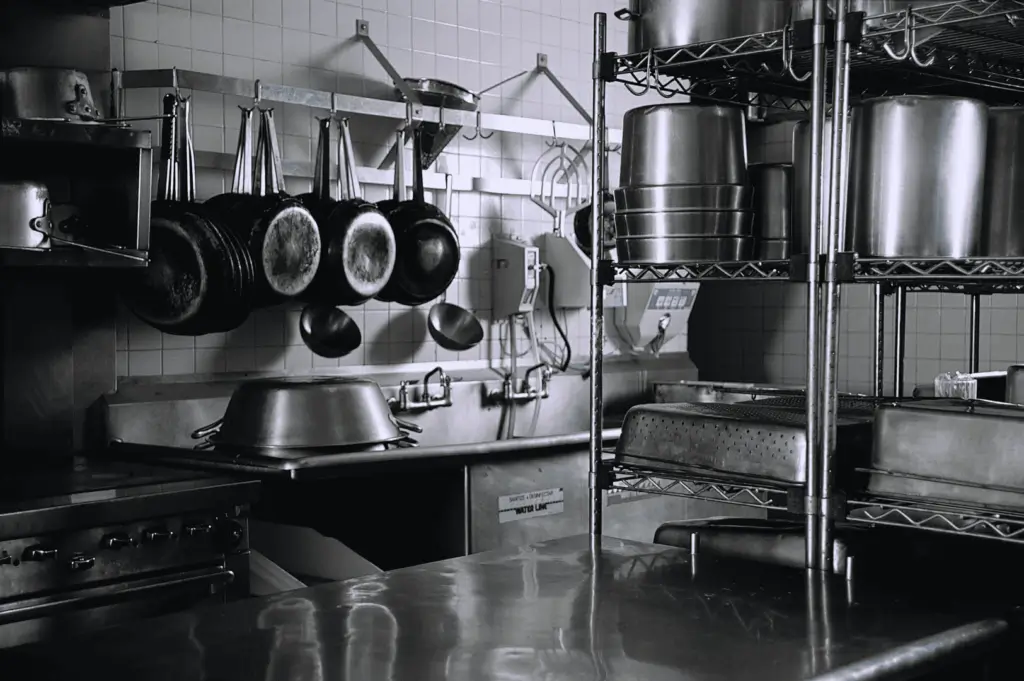 Professional kitchen with stainless steel countertops, hanging cookware, and organized shelving; a clean, ergonomic layout showcasing efficient storage and accessible tools for high-volume culinary production.