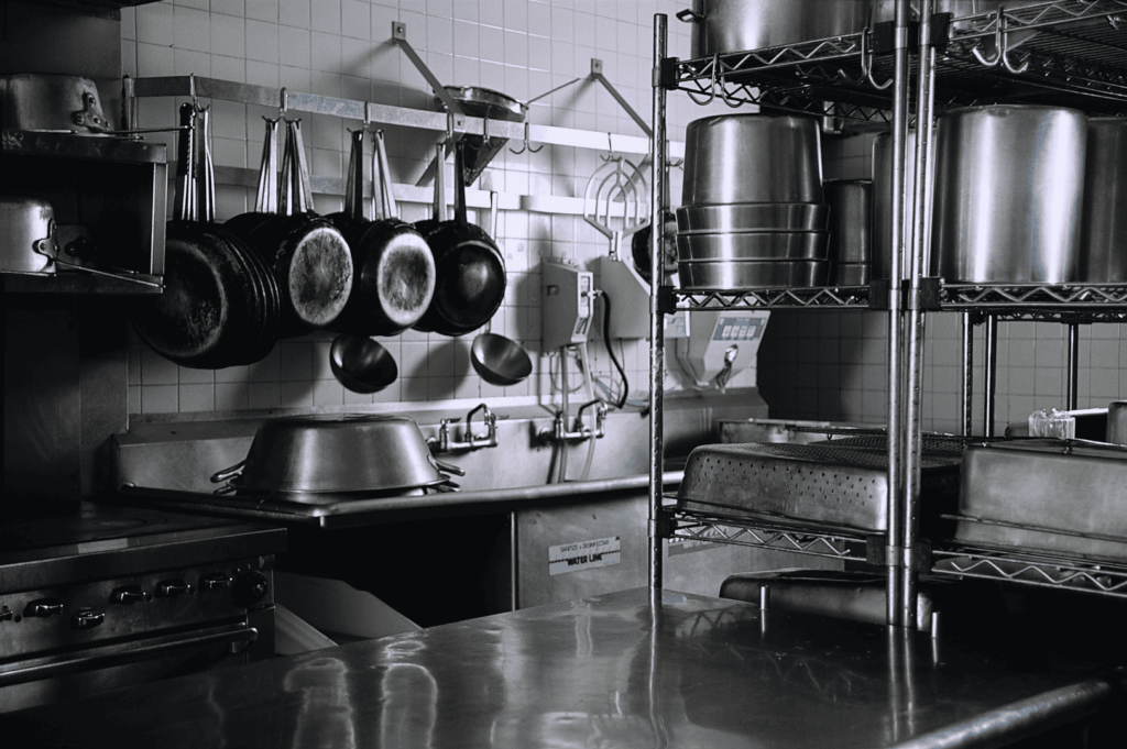 Professional kitchen with stainless steel countertops, hanging cookware, and organized shelving; a clean, ergonomic layout showcasing efficient storage and accessible tools for high-volume culinary production.