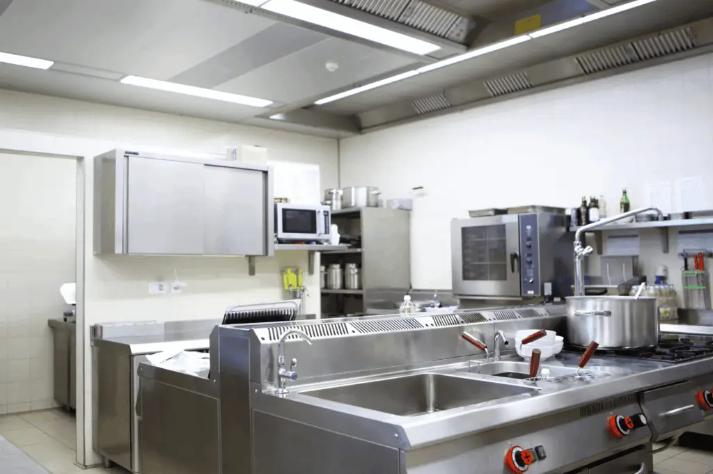Modern commercial kitchen featuring a double sink with red-handled faucets, stainless steel appliances, and neatly arranged cookware; a clean, well-lit space designed for streamlined food prep and professional efficiency.