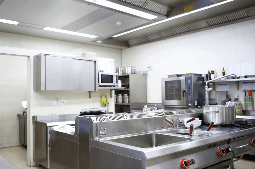 Modern commercial kitchen featuring a double sink with red-handled faucets, stainless steel appliances, and neatly arranged cookware; a clean, well-lit space designed for streamlined food prep and professional efficiency.