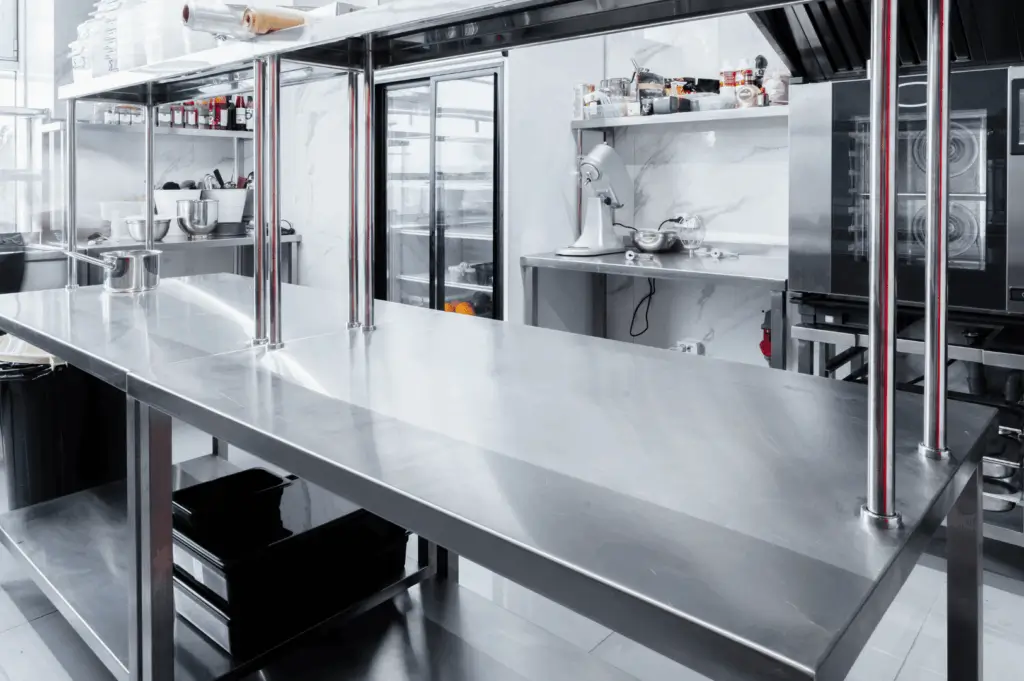 Sleek commercial kitchen with a central stainless steel worktable, surrounded by organized shelves, appliances, and natural light; a hygienic, functional space engineered for seamless culinary workflow and professional precision.