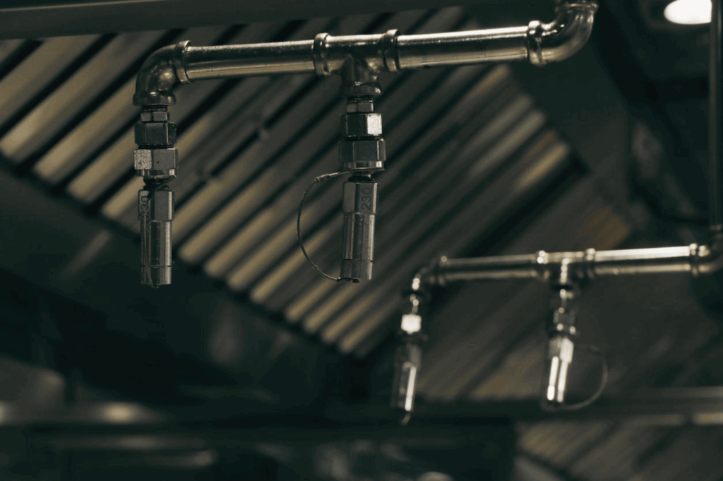 Overhead fire suppression system installed above a cooking station in a Singapore commercial kitchen, featuring metal nozzles and piping integrated into a stainless steel ventilation hood—highlighting essential fire safety measures in high-heat, high-humidity culinary environments.