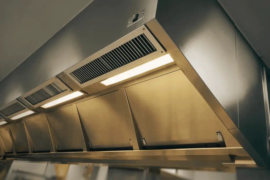 Stainless steel commercial kitchen ventilation hood with angled grease filters and built-in lighting, designed to capture smoke, heat, and airborne grease—illustrating essential airflow solutions for Singapore’s humid culinary environments.