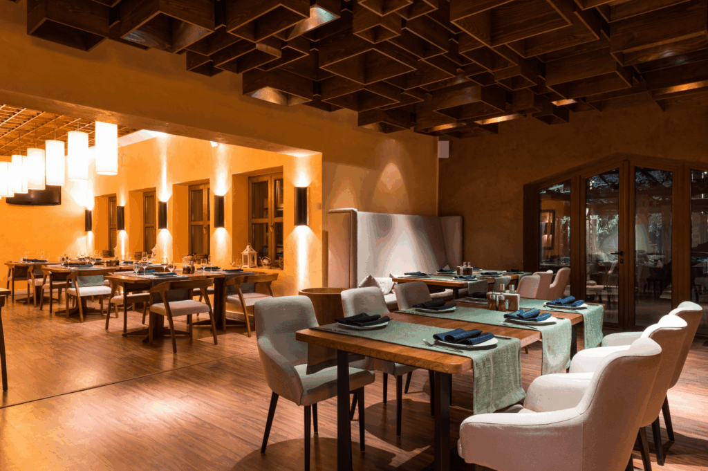 Modern restaurant interior reflecting brand identity through geometric woodwork, warm earth tones, and ambient pendant lighting; green table runners and minimalist decor convey a balance of natural elegance and curated hospitality experience.
