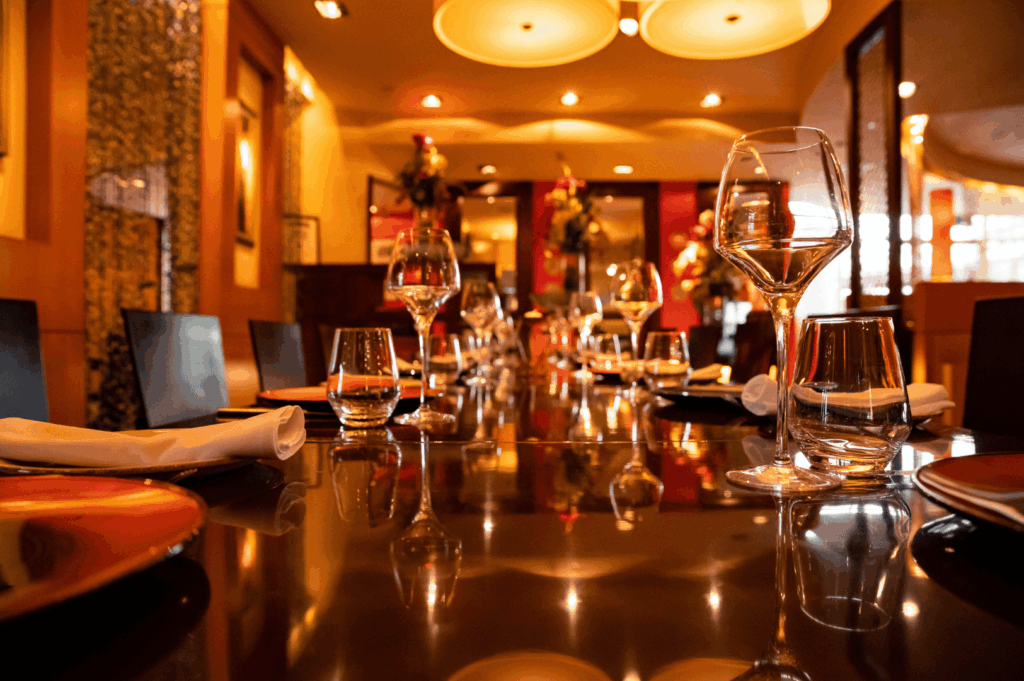Fine dining table set beneath warm ambient lighting, expressing brand identity through elegant glassware, crisp white napkins, and floral accents; the intimate atmosphere and curated decor reflect a hospitality concept rooted in refinement and emotional warmth.