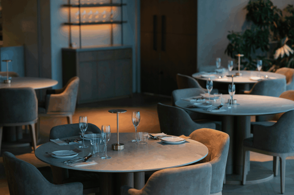Upscale restaurant interior expressing brand identity through minimalist elegance and intimate lighting; round tables with soft-toned upholstery, curated glassware, and subtle greenery evoke a calm, refined hospitality concept grounded in comfort and sophistication.
