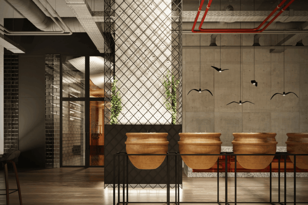 Industrial-style restaurant interior blending raw textures with artistic flair; terracotta pots on a black metal stand anchor the foreground, while a mesh-wrapped column glows softly, sprouting greenery at its base. Exposed concrete walls, red piping, and ductwork emphasize the space’s raw architectural bones. Suspended black bird sculptures add a whimsical contrast, and warm wood flooring softens the starkness. A visual narrative of transformation—where industrial grit meets curated design.