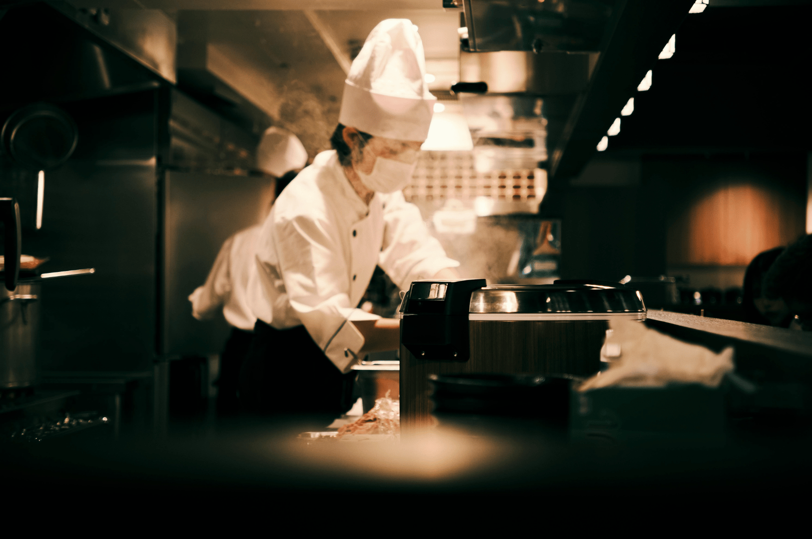 Professional chefs working efficiently in a compact, high-end Singapore kitchen, showcasing smart use of vertical storage, under-counter organization, and streamlined equipment layout—demonstrating how even limited spaces can support dynamic culinary operations.