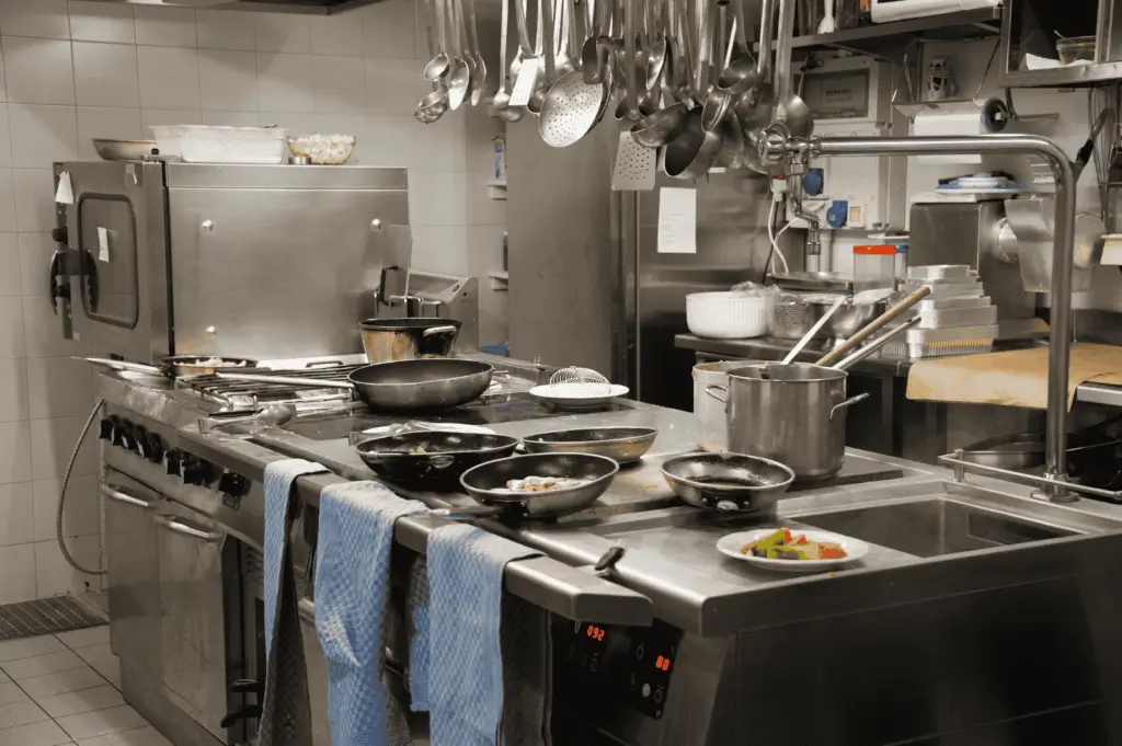 Compact professional kitchen in Singapore featuring stainless steel cooking stations, overhead utensil racks, and efficient under-counter storage—illustrating how thoughtful layout and vertical organization can maximize space in small culinary environments.