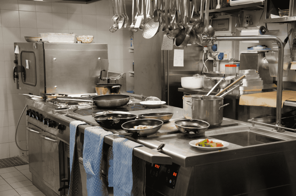 Compact professional kitchen in Singapore featuring stainless steel cooking stations, overhead utensil racks, and efficient under-counter storage—illustrating how thoughtful layout and vertical organization can maximize space in small culinary environments.
