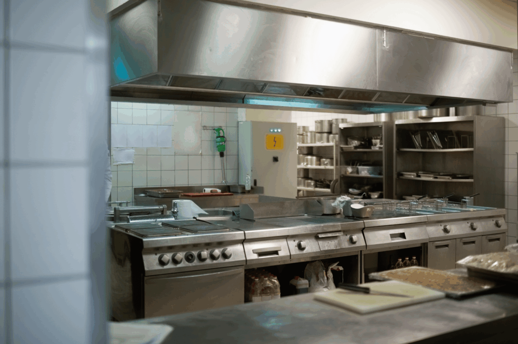 Well-organized commercial kitchen in Singapore featuring stainless steel appliances, overhead shelving, and compact cooking stations—demonstrating how strategic layout and vertical storage solutions can optimize functionality in small professional kitchens.