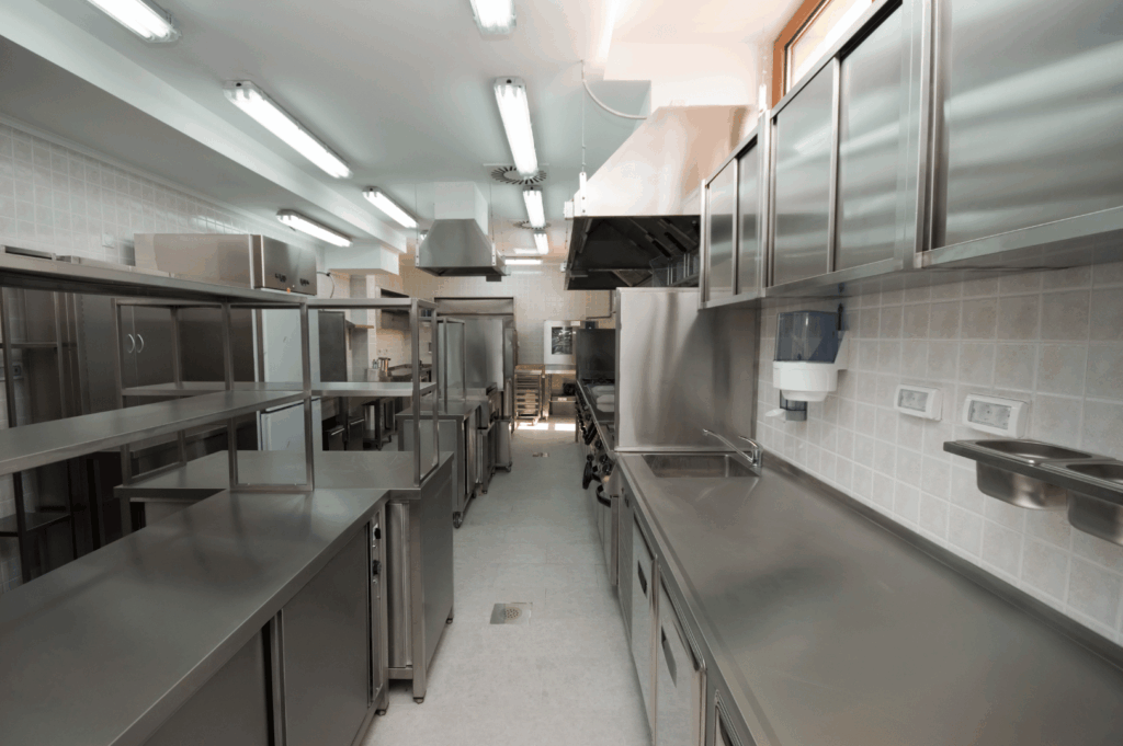 High-volume commercial kitchen in Singapore with stainless steel counters, industrial-grade appliances, and wall-mounted storage—showcasing how clean design, bright lighting, and integrated fixtures can maximize space and efficiency in small-scale culinary operations.