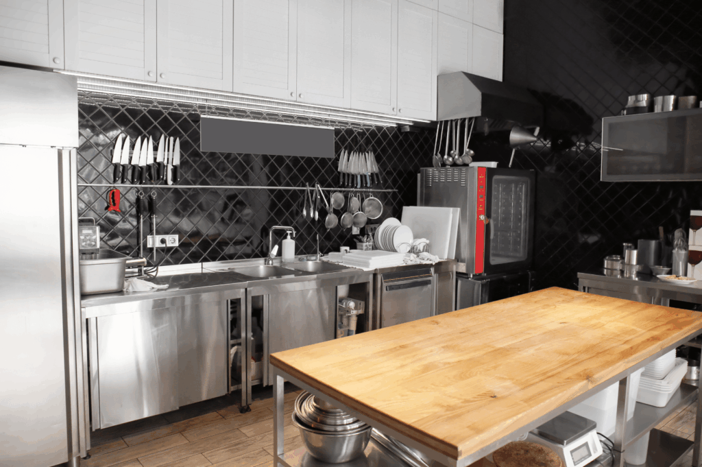 Modern commercial kitchen in Singapore featuring stainless steel surfaces, a central wooden prep island, and wall-mounted storage—illustrating how mixed materials, vertical organization, and efficient zoning can elevate functionality in small kitchen spaces.