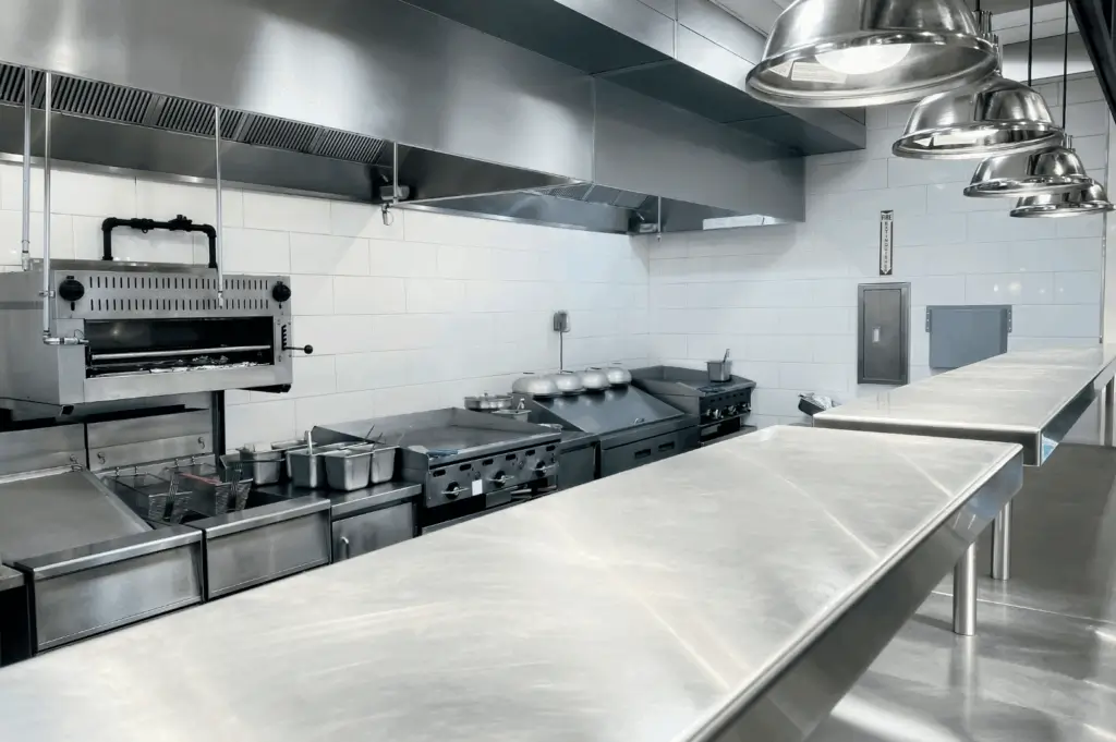 Wide view of a modern commercial kitchen in Singapore with stainless steel counters, bright task lights, and organized appliances, highlighting a clean, efficient workspace for staff comfort.