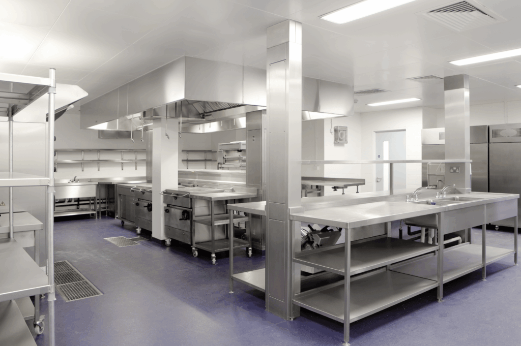 Modern stainless-steel commercial kitchen with wide aisles and ventilation hoods, designed for staff comfort and efficient workflow in a Singapore setting.