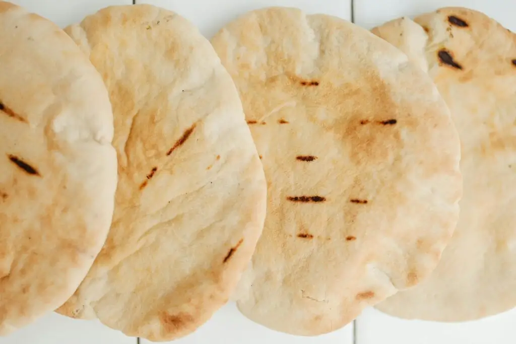 A close-up photo of multiple pita breads overlapping one another as it lays on a white tiled countertop.