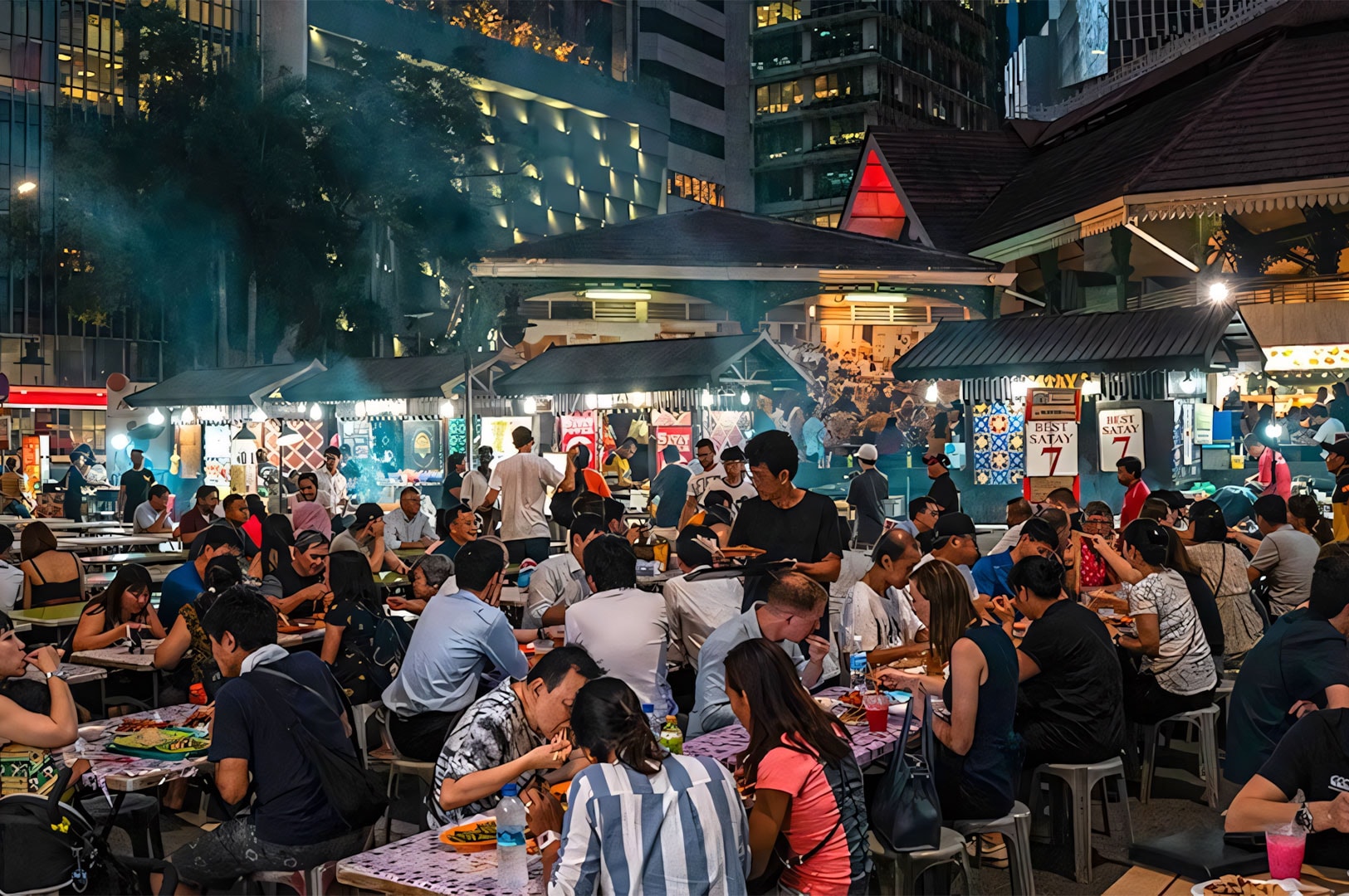 A bustling outdoor night market and hawker center scene at night, filled with crowds eating at communal tables, with smoke rising from busy satay grill stalls in the background.