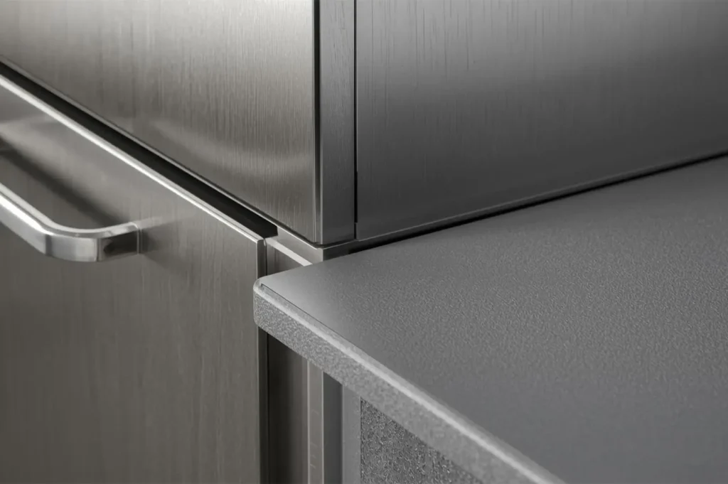 Close-up detail of modern kitchen design, showing the seamless junction between brushed stainless steel or metal cabinetry and a speckled gray countertop with a rounded edge.