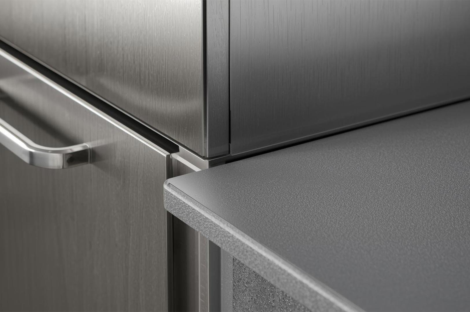 Close-up detail of modern kitchen design, showing the seamless junction between brushed stainless steel or metal cabinetry and a speckled gray countertop with a rounded edge.