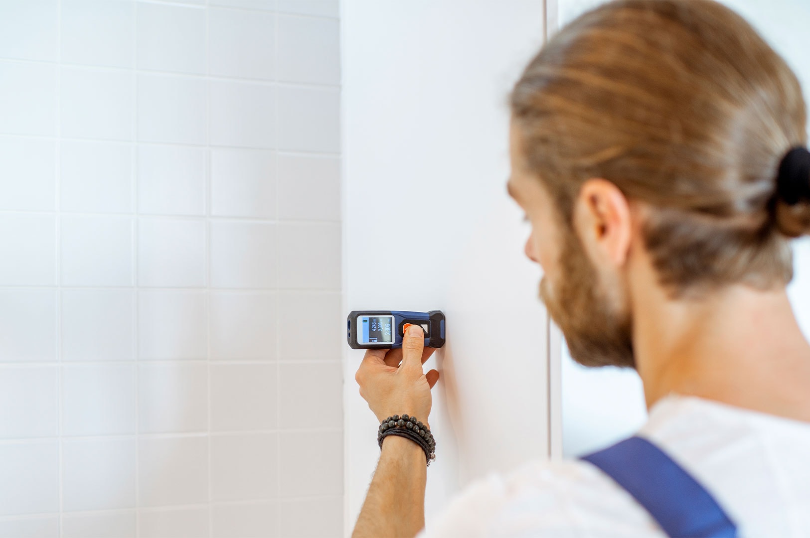 A contractor using a digital laser distance measuring tool against a white tiled wall to ensure accurate dimensions during the bathroom installation process.