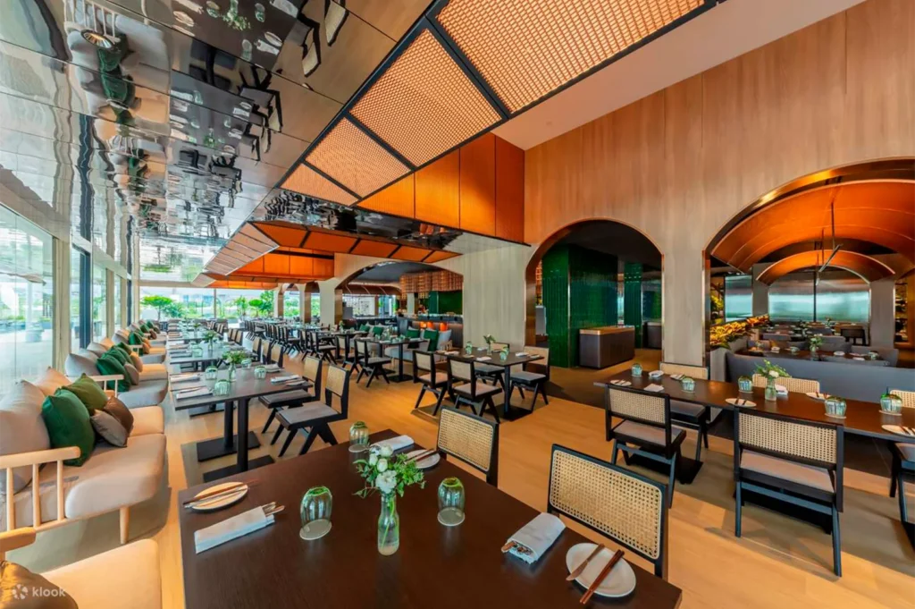 Interior of a modern luxury restaurant with dark wood tables, woven chairs, and a reflective ceiling.