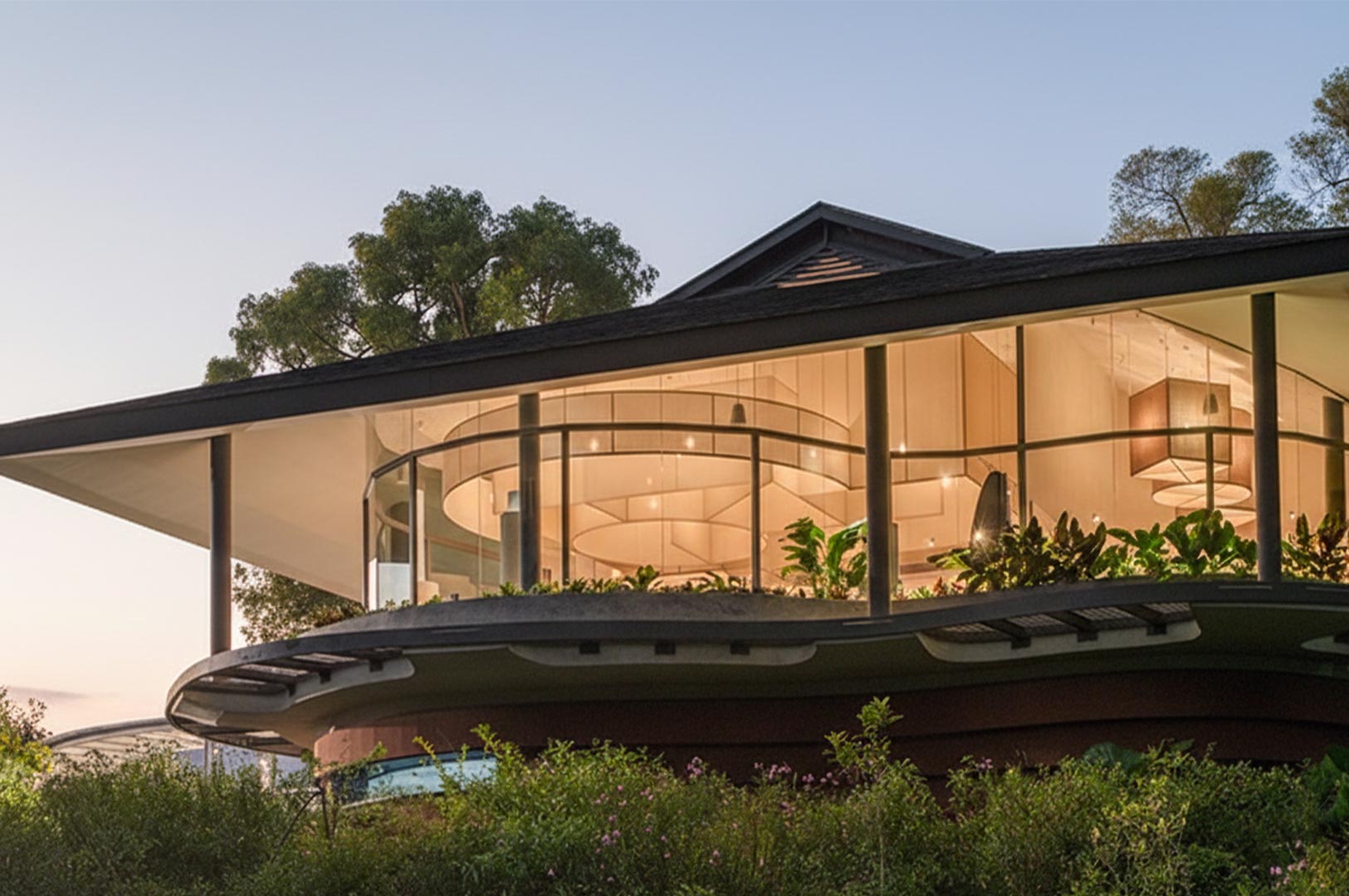 Exterior view of a modern restaurant with a curved glass facade and a sloping roof, nestled in lush greenery under a twilight sky.