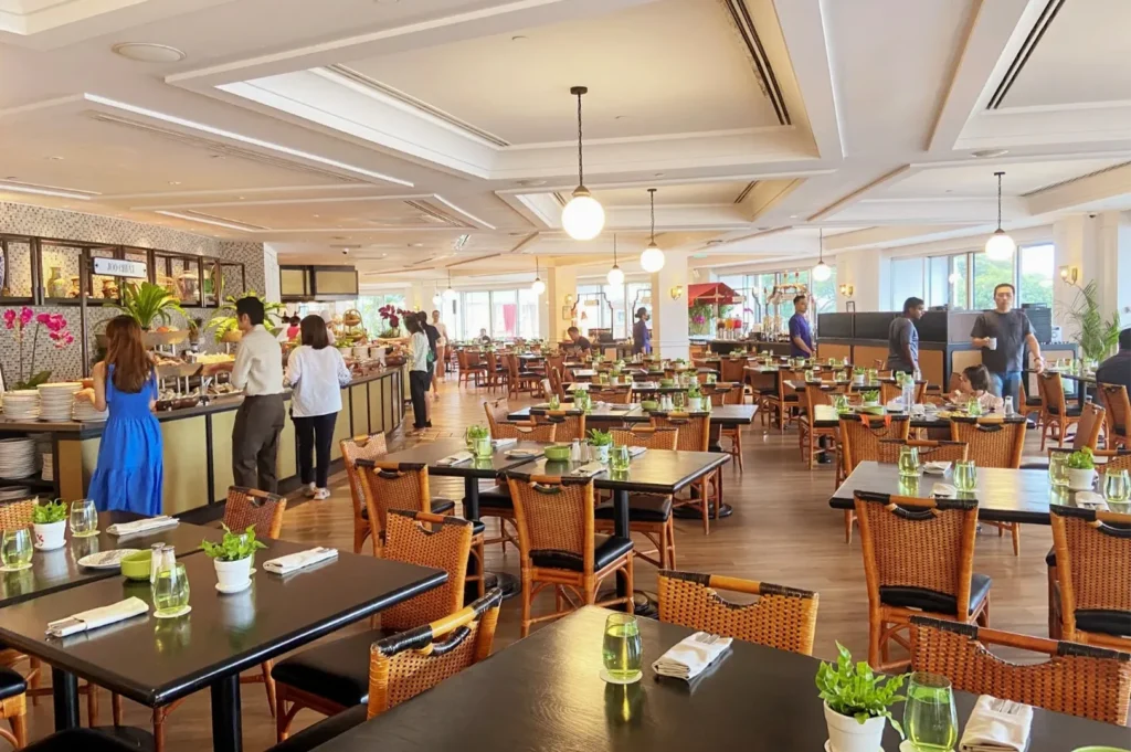 Wide view of a bright, spacious hotel buffet dining room with elegant wooden furniture and hanging globe lights.