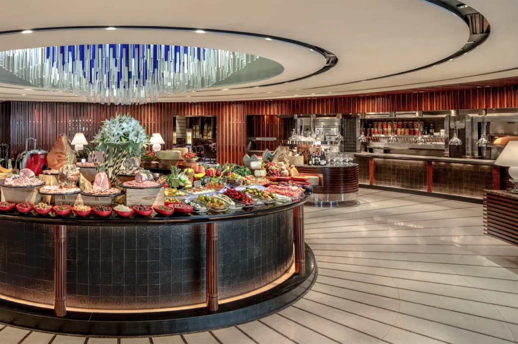 A circular gourmet deli station showcasing a variety of cured meats, cheeses, and fresh vegetables under a crystal chandelier.
