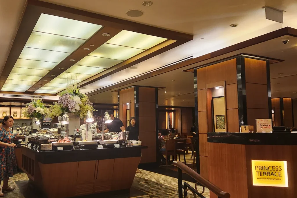 Princess Terrace Authentic Penang Cuisine restaurant buffet area featuring a wide selection of dishes under heat lamps, floral arrangements, and patrons in a warm-lit upscale dining room.