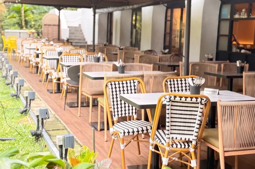 Outdoor restaurant patio with rows of woven black and white checkered bistro chairs and wooden dining tables under an awning.