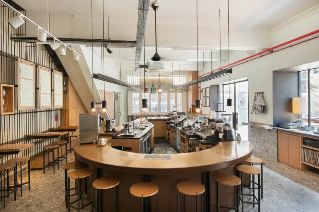 An indoor view of a modern espresso bar featuring a curved wooden counter and minimalist industrial lighting.