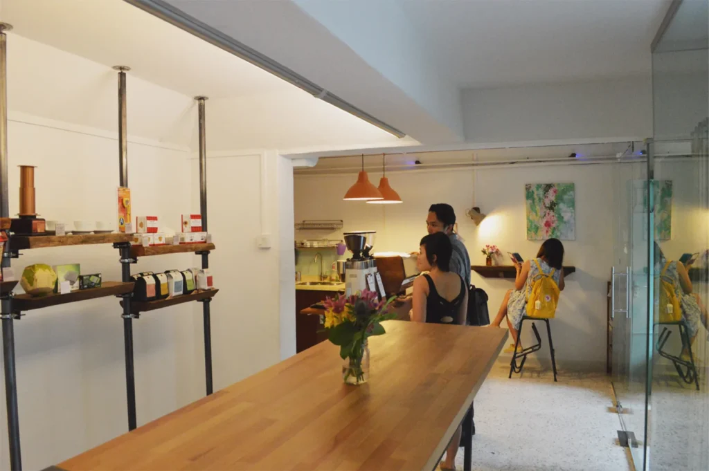 Interior of a boutique coffee shop showing a wooden communal table and retail shelves with coffee beans.