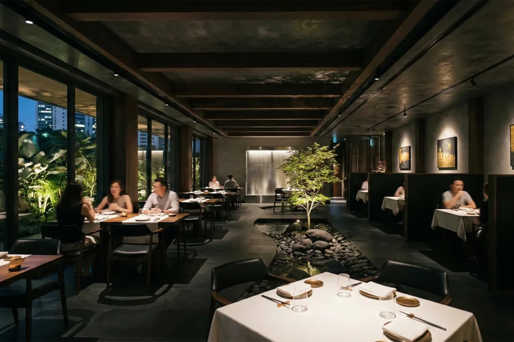 Luxury restaurant dining area with a central indoor rock garden, bonsai tree, and ambient warm lighting.