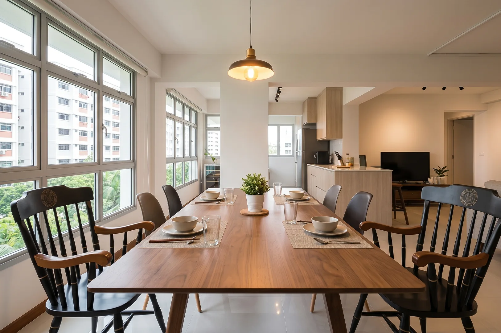 Modern open-concept dining room featuring a long wooden table set with minimalist dinnerware, flanked by black wooden spindle armchairs and brown side chairs under a warm pendant light.