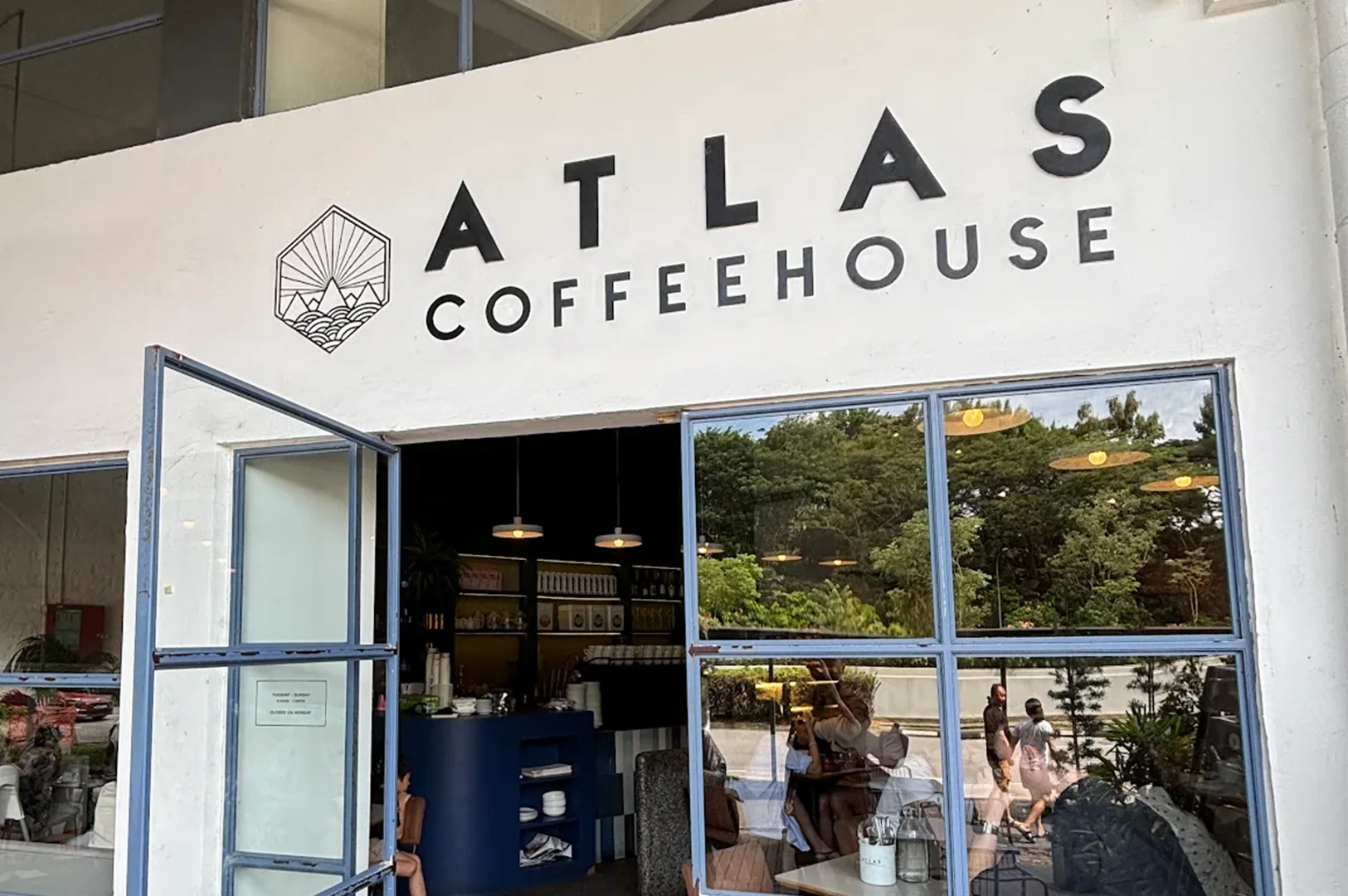 Exterior view of Atlas Coffeehouse showing the minimalist white facade, large windows, and official logo signage above the entrance.
