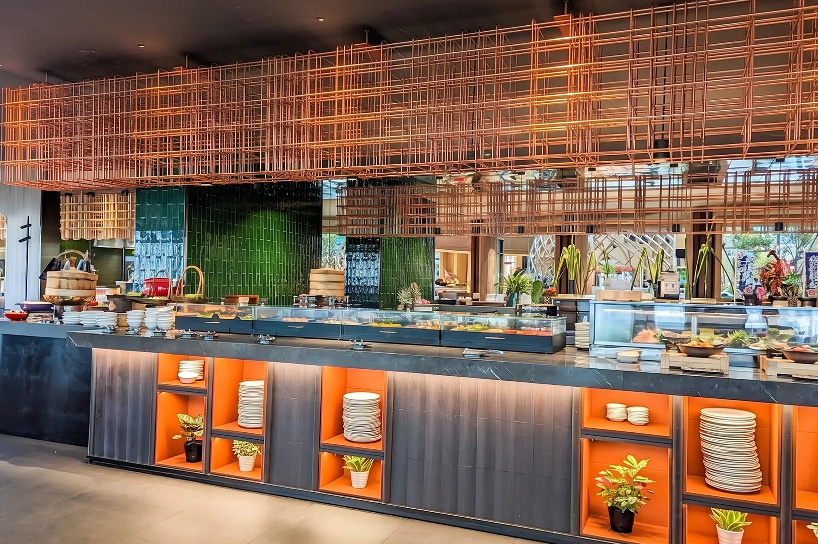 Modern interior of Peppermint restaurant featuring a long buffet counter with orange lit shelving and a decorative copper wire overhead installation.