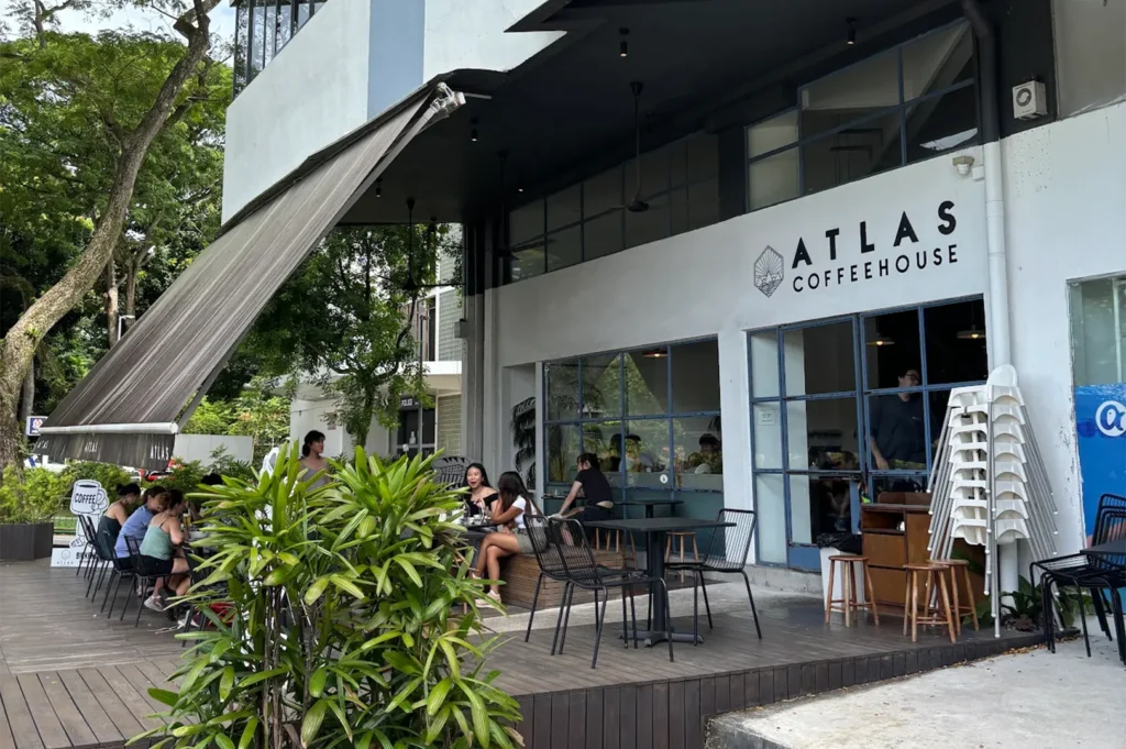Patrons enjoying coffee at the outdoor wooden deck seating area of Atlas Coffeehouse under a large grey awning.