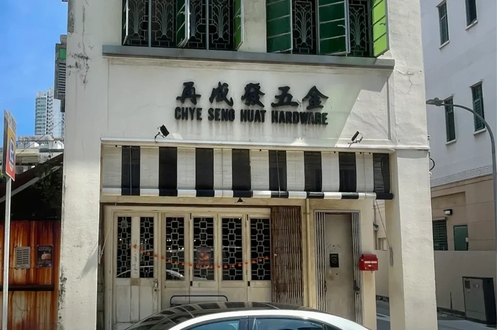 Close-up of the vintage facade and signage of Chye Seng Huat Hardware cafe, featuring traditional metal gates and green shutters.