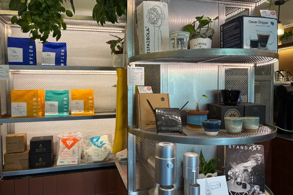 Retail display shelves at Nylon Coffee Roasters showcasing colorful bags of single-origin coffee beans, paper filters, and brewing equipment.
