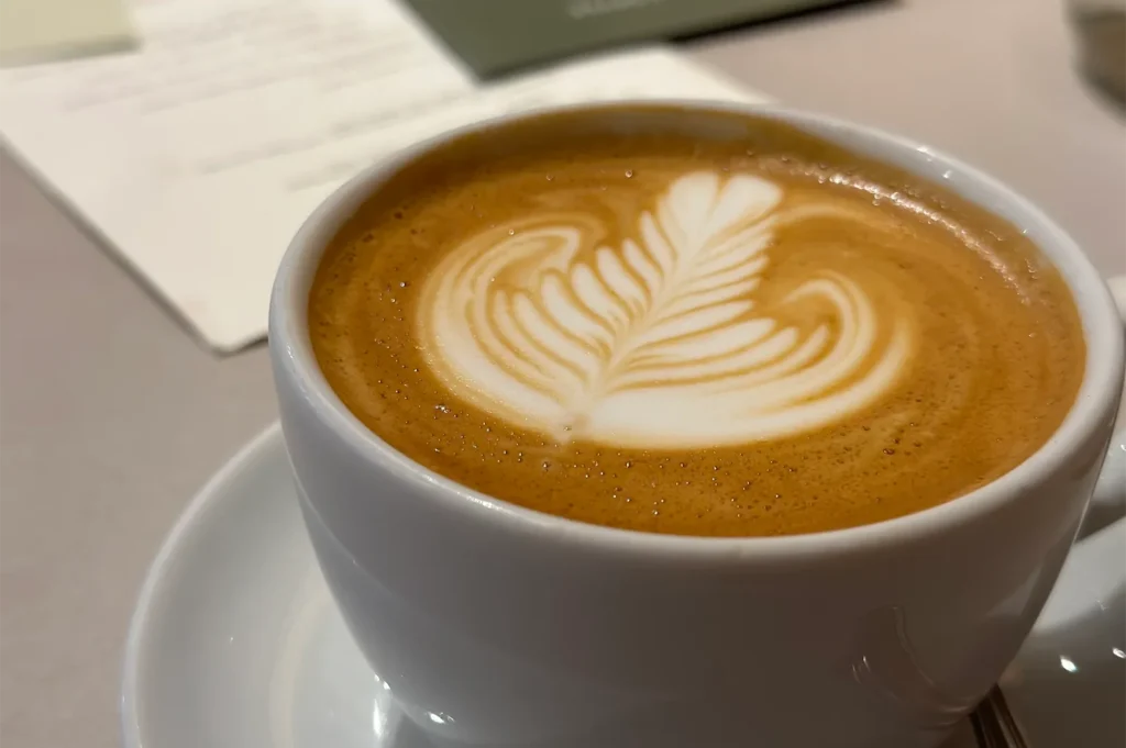 Close-up shot of a creamy latte with detailed leaf pattern latte art in a white ceramic cup at Atlas Coffeehouse.