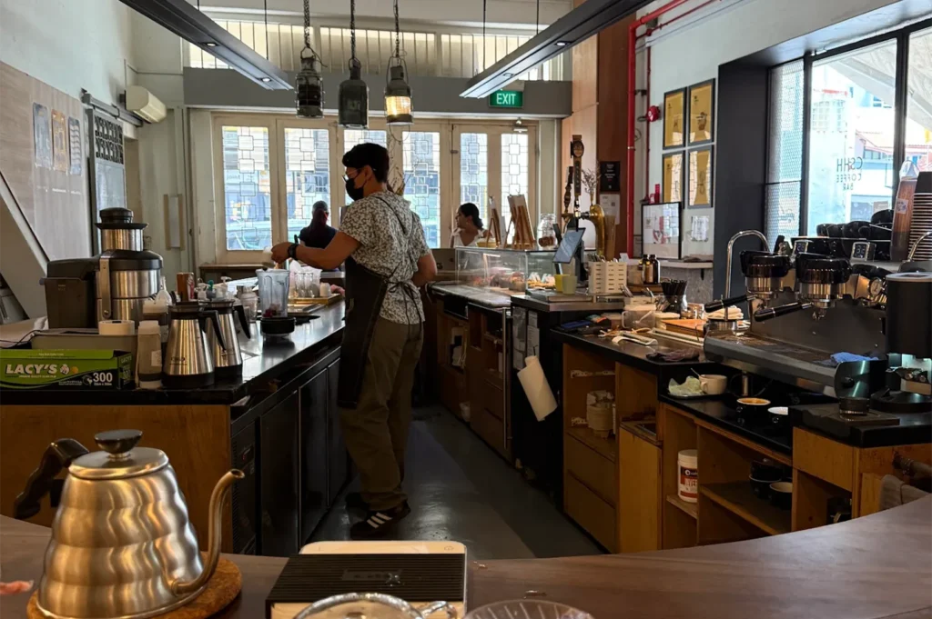 The interior of Chye Seng Huat Hardware coffee bar showing a barista preparing drinks behind a modern industrial counter.