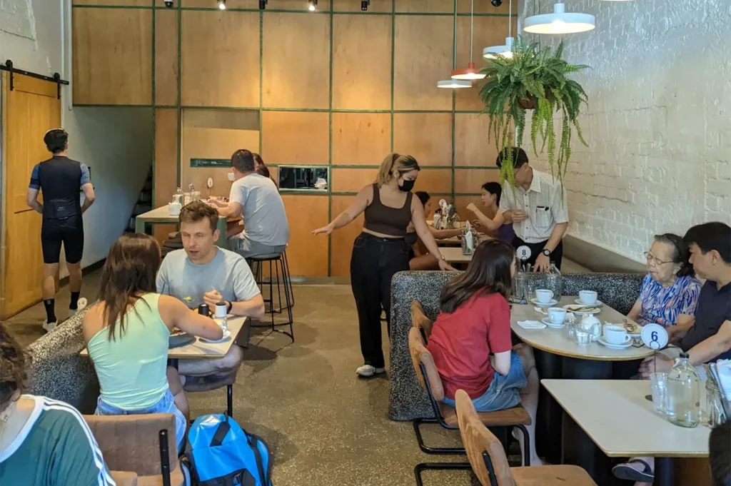 Busy interior of Atlas Coffeehouse featuring warm wood paneling, white brick walls, hanging plants, and customers dining at tables.