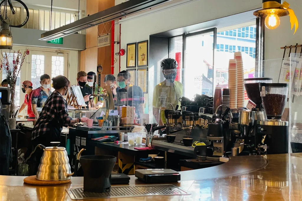 Customers waiting at the service counter of Chye Seng Huat Hardware cafe with professional espresso machines and coffee equipment visible.