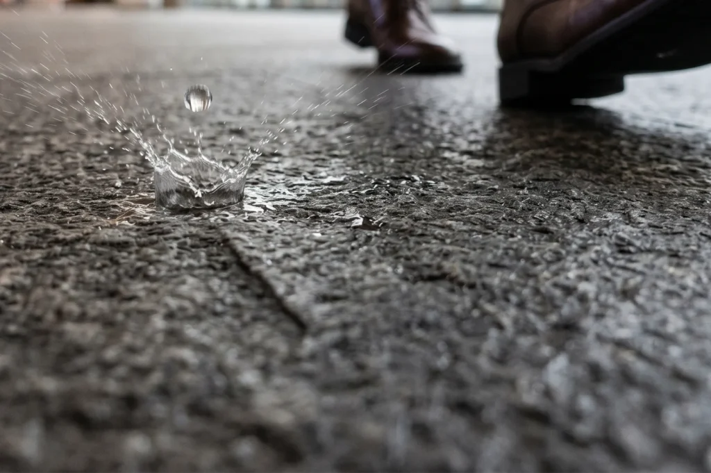 Macro action shot of a water droplet splashing onto a freshly sealed concrete or stone waterproofed surface, demonstrating effective liquid repellency.