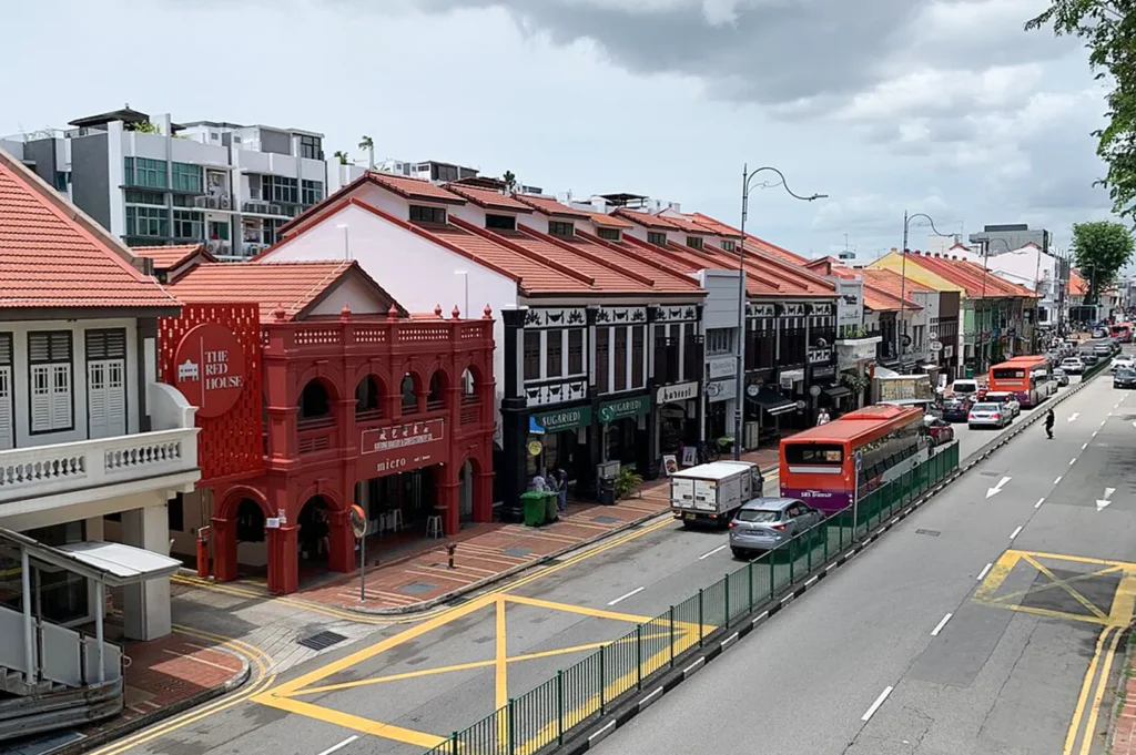 An elevated street view of East Coast Road in Katong, Singapore, showcasing the iconic historic Red House building alongside traditional heritage shophouses and passing traffic.