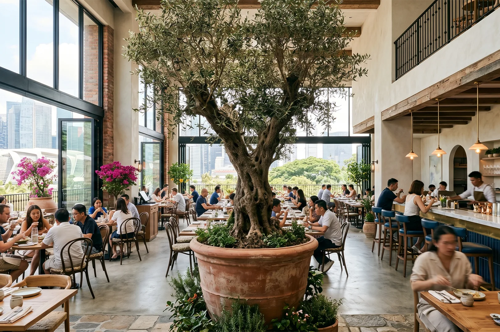 Spacious Mediterranean restaurant interior featuring a large potted olive tree centerpiece, warm wooden tables, and expansive floor-to-ceiling windows with a city skyline view.