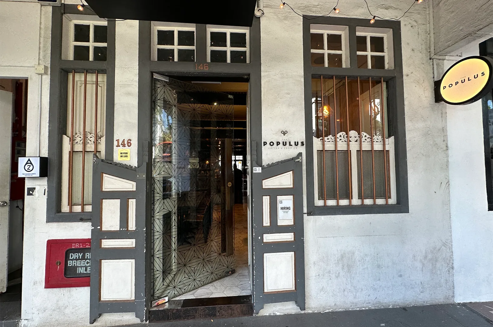 The external storefront and geometric glass entrance of The Populus Coffee & Food Co cafe with a circular illuminated hanging sign.
