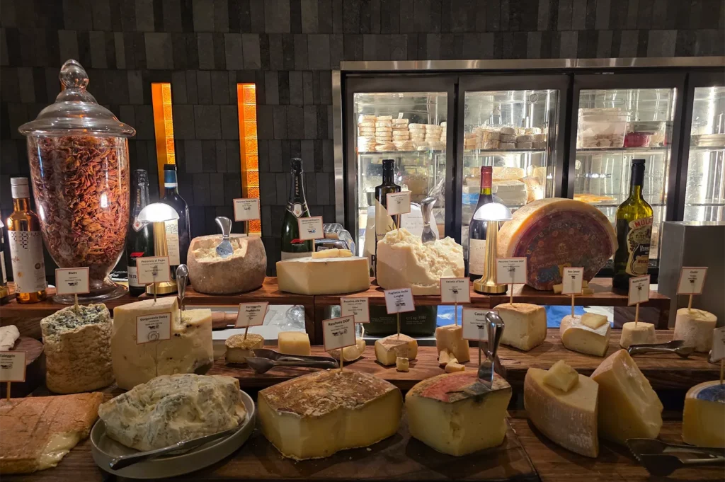 Gourmet Italian cheese buffet display at Basilico featuring various aged cheeses like Pecorino, Gorgonzola Dolce, and Taleggio served with wine and condiments on a rustic wooden counter.