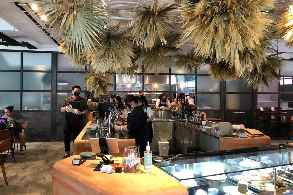 The bustling main coffee counter and pastry display case at Five Oars Coffee Roasters, featuring hanging dried botanical ceiling decorations and baristas preparing drinks.
